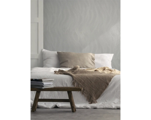 Schlafzimmer mit Bett, Tagesdecke, Kissen, Bücherstapel und Tapete mit Wellenmuster