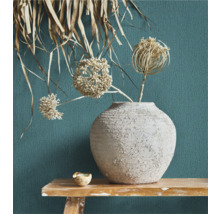 Dekorative Blumenvase mit Trockenblumen auf einem Holztisch vor einer strukturierten Wand