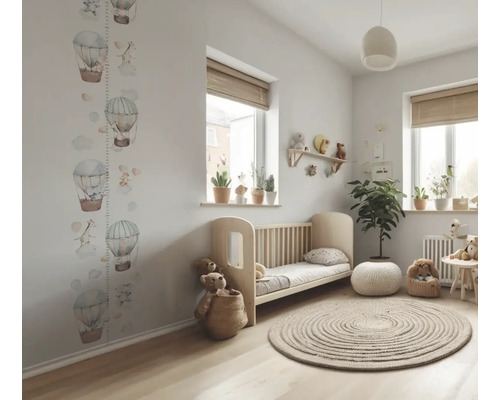Kinderzimmer mit Babybett, rundem Teppich, Fenster mit Rollo und Wachstumsmesser mit Luftballonmotiven an der Wand