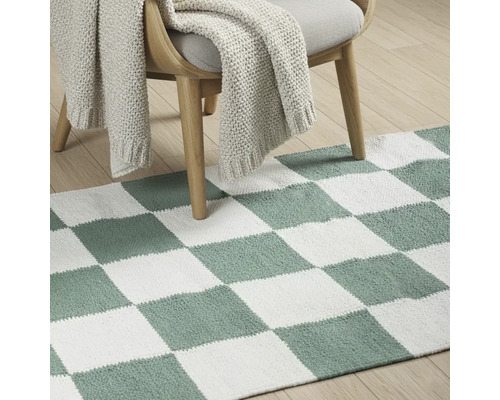 Dekorative Bodenszene mit Teppich im Schachbrettmuster unter einem Stuhl mit Strickdecke.