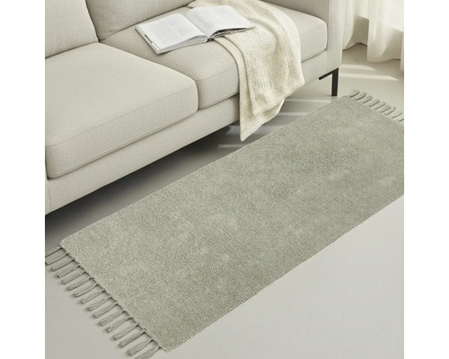 Grauer Teppichläufer mit Fransen neben einem Sofa mit Buch