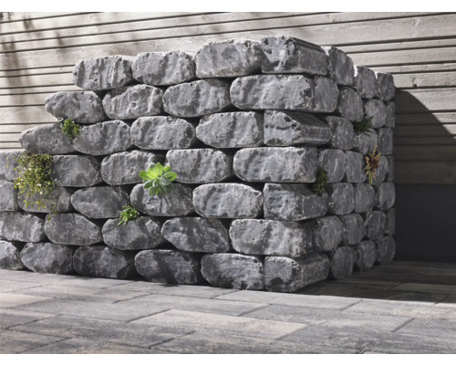 Gestapelte graue Pflanzsteine mit Bepflanzung vor einer Holzwand