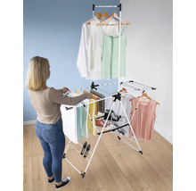 Eine Frau hängt Wäsche auf einem weißen, mehrstöckigen Wäscheständer mit Kleidung und Handtüchern.