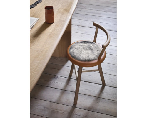 Holzstuhl mit rundem Sitz und Fellauflage neben Holztisch