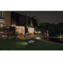 Rasenmähroboter bei der Nachtarbeit in einem Garten mit Haus und Pool.