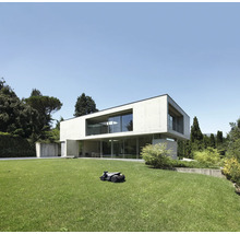 Rasenmähroboter auf Rasen vor modernem Haus