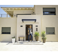 Modernes Haus mit hellen Fassaden, grauen Rolläden, einem schwarzen Vordach über der Haustür und großen Pflanzgefäßen im Eingangsbereich.