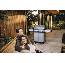 Paar entspannt auf einer Bank im Freien mit einem Gasgrill im Hintergrund.