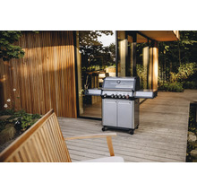 Gasgrill auf einer Terrasse mit Holzdeck und einem Gebäude im Hintergrund.