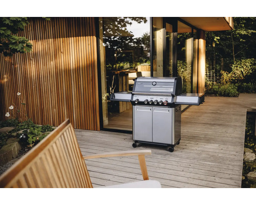 Gasgrill auf einer Terrasse mit Holzdeck und einem Gebäude im Hintergrund.