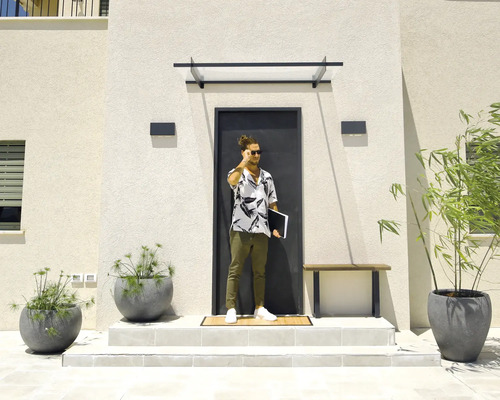 Moderner Hauseingang mit dunkler Tür, Glasvordach, rechteckigen Außenwandleuchten und großen grauen Pflanzkübeln auf hellen Stufen.