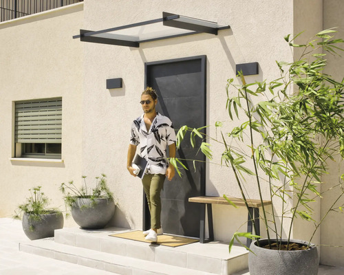 Moderner Eingangsbereich mit schwarzem Vordach, einer minimalistischen schwarzen Haustür und Pflanzkübeln auf einer hellen Terrasse.