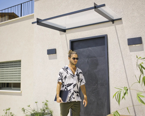 Modernes Haustürvordach mit schwarzem Metallrahmen und transparenter Abdeckung über einem dunklen Hauseingang an einer hellen Fassade.