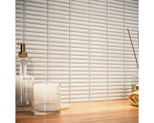 Szene mit weißen, länglichen Wandfliesen, Seifenspender, Kerze und Handtuch auf einem Holztisch