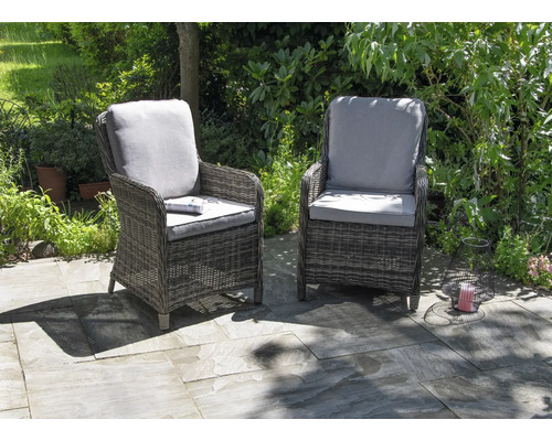 Zwei Rattan-Gartenstühle mit Kissen stehen auf einer Terrasse.