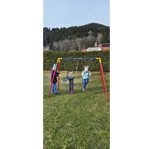 Szene mit drei spielenden Kindern auf einer Metallschaukel im Garten