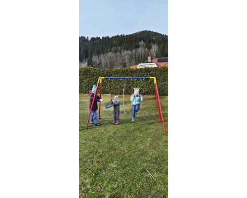 Szene mit drei spielenden Kindern auf einer Metallschaukel im Garten