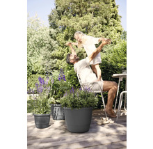 Vater und Tochter spielen im Garten neben Pflanzgefäßen auf einer Holzterrasse