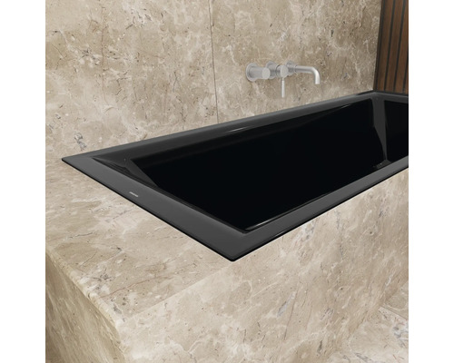 Schwarze Badewanne mit Armatur in einem Badezimmer mit Marmorwänden.