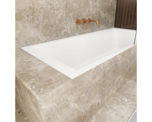 Eingebaute Badewanne in einem Badezimmer mit Marmorverkleidung und Armatur.
