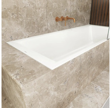 Eingebaute Badewanne mit Marmorverkleidung und Armatur an der Wand.