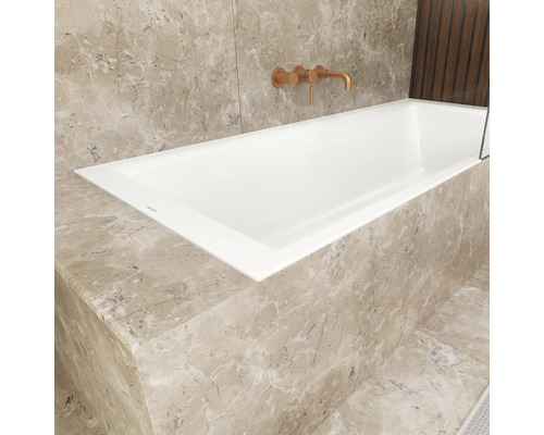 Eingebaute Badewanne mit Marmorverkleidung und Armatur an der Wand.