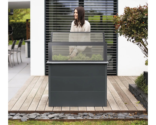 Hochbeet mit transparentem Aufsatz und Frau bei der Gartenarbeit auf einer Holzterrasse