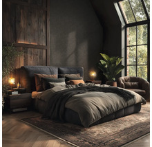 Schlafzimmer mit Bett, Nachttischen, Lampen, Teppich und Sessel in dunklen Farben