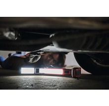 Eine Person liegt unter einem Auto und verwendet eine Arbeitsleuchte für Reparaturen.