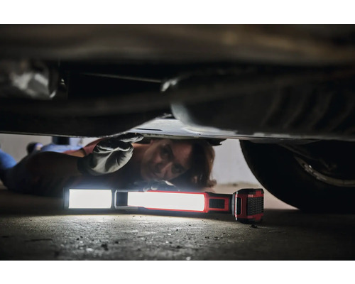 Eine Person liegt unter einem Auto und verwendet eine Arbeitsleuchte für Reparaturen.