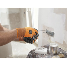 Eine Person befestigt mit einem Schraubenzieher eine Halterung an einer Wand. Auf einem Tisch stehen ein Schwamm, eine Dose und ein Pinsel.