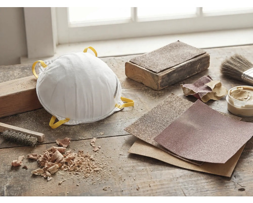 Staubmaske, Schleifpapier und Werkzeuge auf einer Werkbank