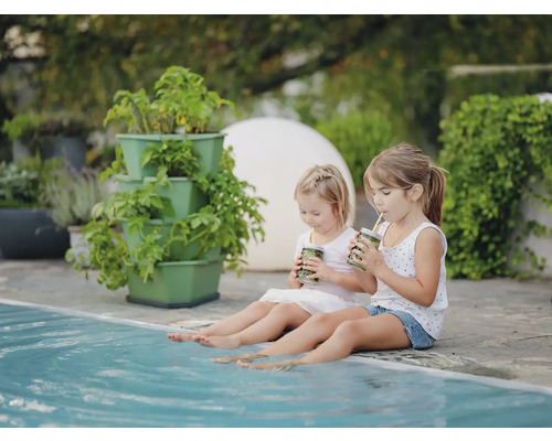 Zwei Mädchen sitzen am Pool mit Getränken und blicken auf einen Pflanzturm mit Pflanzen.