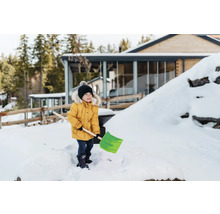 Ein Kind mit einer Schneeschaufel im verschneiten Garten eines Hauses