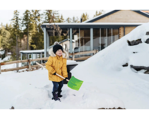 Ein Kind mit einer Schneeschaufel im verschneiten Garten eines Hauses
