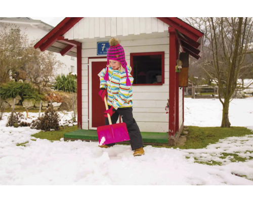 Mädchen schaufelt Schnee vor einem Spielhaus im Garten