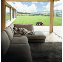 Szene mit Junge, der auf einem Sofa liegt, während ein Mähroboter im Garten arbeitet