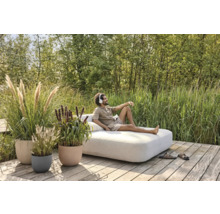 Szene im Garten mit einem Mann, der auf einem Lounge-Sofa liegt, umgeben von Ziergräsern in Pflanzgefäßen.