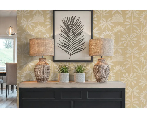 Dekoratives Interieur mit zwei Lampen, zwei Zimmerpflanzen, einem gerahmten Bild und einer Kommode vor einer Wand mit Palmenmuster.