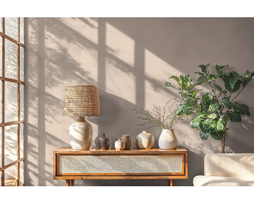 Wohnraum mit Holztisch, Lampe, Vasen und Pflanze vor einer Wand
