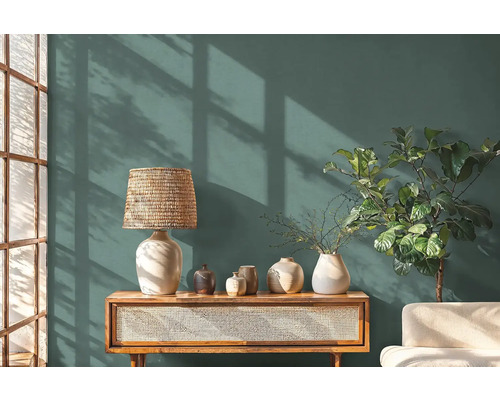 Wohnzimmer mit einer Kommode, einer Lampe, Vasen und einer Zimmerpflanze vor einer Wand