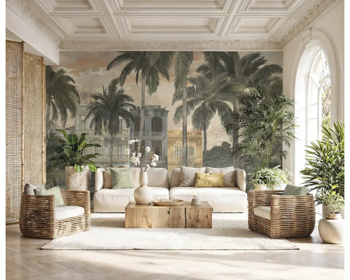 Fototapete mit Palmen und kolonialen Gebäuden in einem hellen Wohnzimmer mit weißem Sofa, Korbsesseln und Holz-Couchtisch.