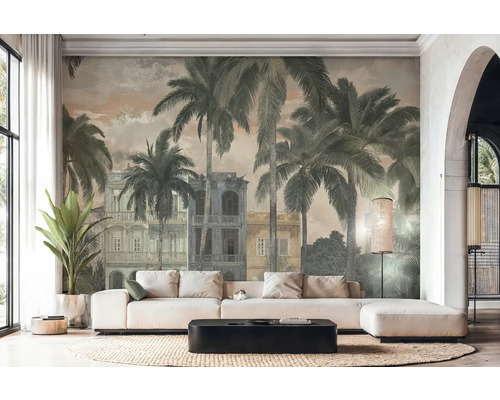Helles Wohnzimmer mit Fototapete im Vintage-Stil, die Palmen und koloniale Gebäude zeigt. Weißes Ecksofa, schwarzer Couchtisch und Flechtteppich.