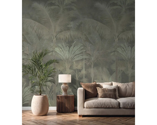 Vliestapete mit Palmenmuster in einem hellen Wohnzimmer hinter einem cremefarbenen Sofa, einer Tischlampe und einer großen Zimmerpflanze.