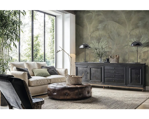 Modernes Wohnzimmer mit heller Couch, Lederhocker und Vliestapete mit Palmenmotiv an der Wand hinter einem Sideboard.