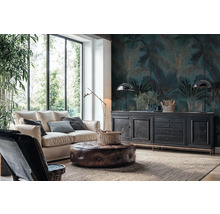 Wohnzimmer mit Fototapete im Palmen-Design in Dunkelblau und Gold, hellem Sofa, Leder-Sitzhocker und schwarzem Sideboard vor großen Fenstern.