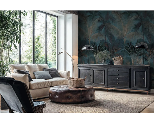 Wohnzimmer mit Fototapete im Palmen-Design in Dunkelblau und Gold, hellem Sofa, Leder-Sitzhocker und schwarzem Sideboard vor großen Fenstern.