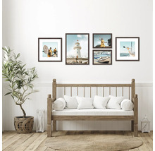 An der Wand hängen fünf gerahmte Küstenbilder über einer Holzbank mit weißen Kissen