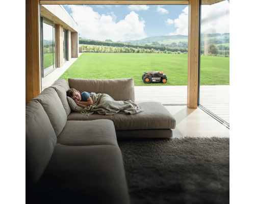 Junge schläft auf Couch, während Rasenmähroboter im Garten arbeitet