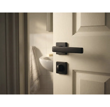 Tür mit schwarzer Türklinke und Badezimmer im Hintergrund